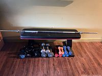 Overall view of Marcy bench with barbell on top, kettlebells and dumbbells arranged underneath