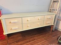 Front view of sage green and cream six-drawer dresser showing tapered legs and pulls