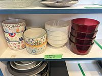 All 13 bowls grouped on shelf: 5 patterned ceramic, 4 white ceramic, 4 red glass