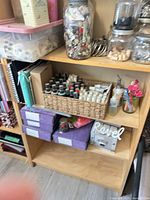 Overall view of shelf with jars of buttons, metal rings, spools, spray bottles in basket, storage binders and other supplies