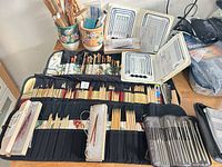 Open roll-up case with numerous straight and double-pointed needles, trays of metal needles, ceramic holders with additional needles