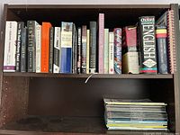 Two-shelf view showing assortment of books and stack of magazines
