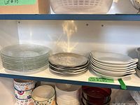 Three stacks of plates on shelf: clear glass, grey metal, white porcelain