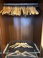 Wide view of closet showing upper rail full of wooden hangers and additional hangers in lower basket