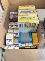 Opened carton showing Xyron cartridge boxes, numerous small adhesive refill boxes, blue dispenser