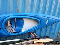 Full view of blue Pelican kayak on side with two paddles beneath