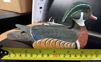 Profile view of carved wood duck decoy with measuring tape showing 7 in length