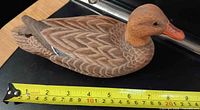 Left side view of carved duck decoy beside tape measure showing length
