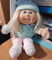Full view of seated Cabbage Patch Kids blond doll on desk