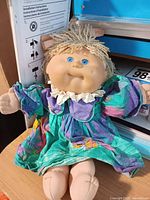 Full view of Cabbage Patch Kids doll sitting, showing dress and body