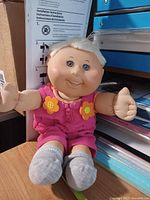 Full view of seated Cabbage Patch Kids doll in pink romper and grey socks