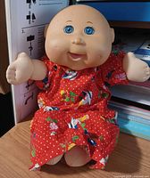 Full view of 12-inch Cabbage Patch Kids Preemie doll seated, wearing red floral dress