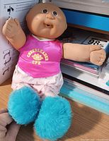 Full view of doll lying on shelf wearing cheerleader outfit and blue booties