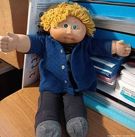 Front view of Cabbage Patch Kids boy doll seated, showing face, clothing, hair