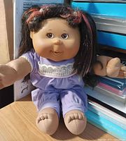 Front view of Cabbage Patch Kids doll seated, showing outfit and hair