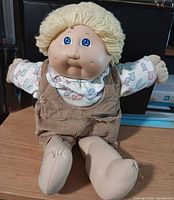 Front view of 16" Cabbage Patch Kids boy doll with blond yarn hair, blue eyes, tan corduroy overalls, patterned shirt