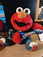 Elmo plush wearing leather jacket holding blue guitar