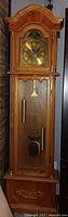 Front view of full grandfather clock showing case, dial, pendulum and weights