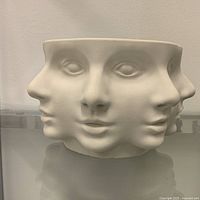 Front view of matte white pedestal bowl with multiple sculpted faces