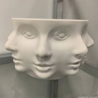 Front view of white ceramic bowl showing three sculpted faces