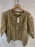 Front view of light brown embellished cardigan on hanger showing buttons, ruffles, beads, tag attached