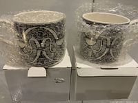 Two ceramic mugs wrapped in bubble wrap sitting on their individual white boxes