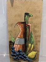 Full view of unframed still life painting showing jug and fruits on canvas board