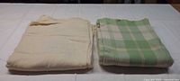 Folded cream and green plaid wool blankets side by side