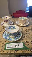 Three floral fine china cup and saucer sets on countertop