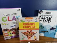 Front view of three boxed kids craft kits: Fun with Clay, Origami Animals, Ultimate Flying Paper Planes
