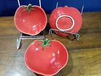 Front and back views of three tomato-shaped bowls showing color, shape, and maker’s mark