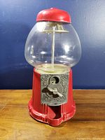 Front view showing red base, glass globe, crank and coin slot