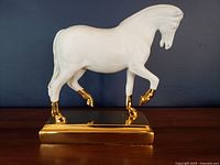 Side view of white resin horse figurine on gold base