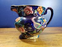 Left side view of cobalt blue jug showing pheasant, flowers, and gilt rim