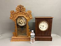 Both mantel clocks side by side with water bottle for scale
