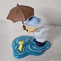 Front view of Pooh figurine with umbrella and duckling on puddle base