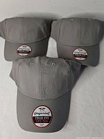 Three gray Imperial True Fit UPF 50+ golf caps, brand stickers on brims