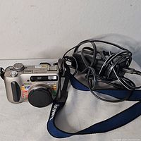 Front view showing camera with lens cap, neck strap, and AC adapter/charger