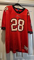 Front view of red Buccaneers #28 Champion jersey on hanger