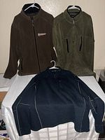 Three jackets displayed on a table, brown, olive, navy.