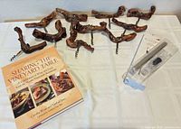 Group shot of ten burlwood corkscrews, wine chiller stick in packaging, and signed cookbook