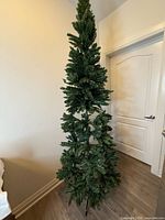 Full view of assembled slim 8ft artificial Christmas tree showing metal stand, green branches