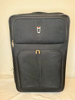 Front view of black Delsey suitcase showing logo patch and front zip compartments