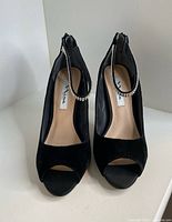 Front view of black suede peep-toe high heels showing rhinestone ankle straps and Nina label