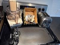 Stovetop view of Cuisinart food processor, box of blades, Cuisinart toaster and Black & Decker griddle