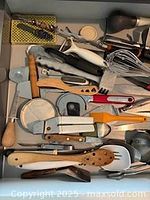 Top view of drawer showing majority of utensils including peelers, wooden spoons, biscuit cutters