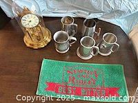 Group shot of clock, five pewter mugs, green bar towel