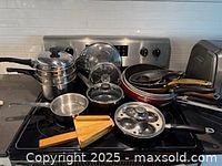 Full lot on stovetop showing steamer, glass lid, stack of frying pans, egg poacher, jar opener
