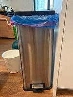 Stainless steel pedal bin with liner bag visible, partial view of white plastic bin
