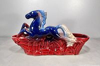 Side view of blue and white galloping horse atop red base planter